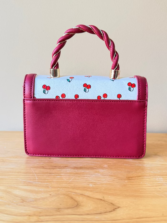 Red and White Handbag with cherry pattern and twisted handle on a wooden surface