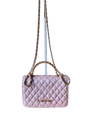 Pink quilted handbag with chain strap on a wooden surface against a beige wall
