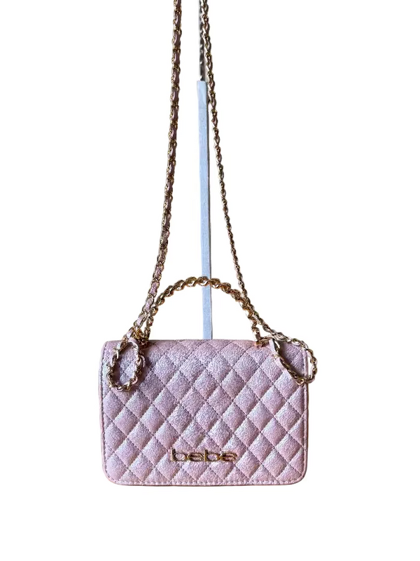 Pink quilted handbag with chain strap on a wooden surface against a beige wall