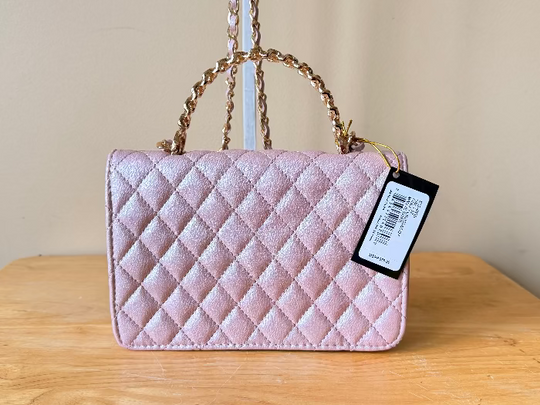 Pink quilted handbag with a tag on a wooden surface