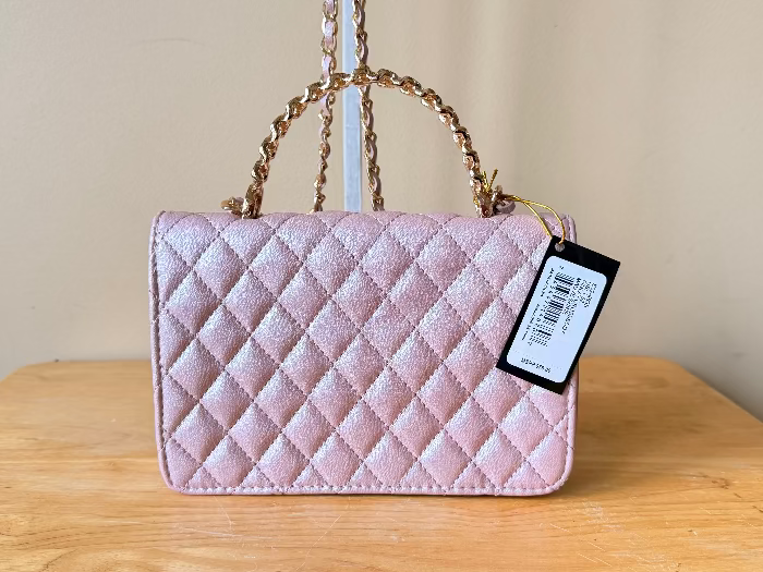 Pink quilted handbag with a tag on a wooden surface