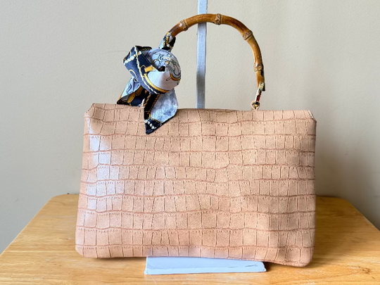 Beige textured handbag with a bamboo handle on a wooden surface against a plain background