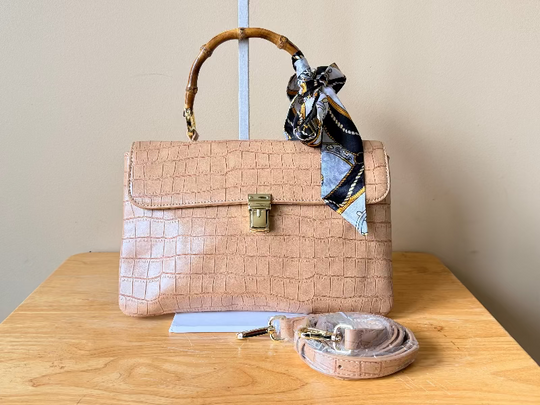 Beige handbag with a matching belt and scarf on a wooden table.
